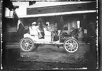 'Diverse fotografier från bl.a. dåvarande Nordrhodesia, nu Zambia, tagna av Konsul Magnus Leijer. ::  :: 3 st män och 1 st kvinna med barn sittande i en bil, bakpå bilen sitter 1 st man med 2 fanor i händerna. Bakom bilen, en häst, hus och 3 st människor.'