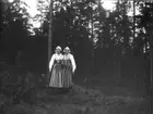 'Bildtext: ''Från Skarsberget.'' :: Vy med 2 kvinnor iklädda dräkter stående på öppen mark med tallvegetation i bakgrunden. ::  :: Ingår i serie med fotonr. 5234:1-12. Se även 5223:1-13, 5231:1-11 och 5232:1-8.'