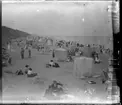 'Bildtext: ''Hornsea bathing beach.'' (Hornsea badstrand) :: Vy över badstrand med människor på stranden. Med kläderna på, sittande i solstolar. På stranden även tält uppsatta. Hattklädda. Barnvagn. :: Kläder. ::  :: Ingår i serie med fotonr 5268:1-13. Se även hela serien med fotonr. 5237-5267.'