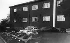 'Göteborgs Naturhistoriska museum oktober 1978: :: Östra tegelväggen av Göteborgs Naturhistoriska Museum. Mur av sten med block av olika bergarter ovanpå. Block framifrån och bakåt:2 stycken orstensbollar, dalasandsten, diorit, morän, kambrisk sandsten, diabasgång i gnejs, rivningsbreccia, Kinnediabas, grå gnejsgrait, ?, dalaporfyr, granatamfibibolit, hornbländit samt ? :: 6 bilar parkerade mellan muren och byggnaden. ::  :: Ingår i serie med fotonr. 5527:69-216.'