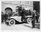 'Zoologiska avdelningens flytt till Naturhistoriska museet i Slottsskogen: Monterade djur lastade på bilflak, stående framför byggnad, för transport till museet i Slottsskogen. Människor samlade runt bilen. Bilhorn synligt. ::  :: Text på baksidan av ett av fotona: ''De vilda djurens nödtvungna gatuparad.'''