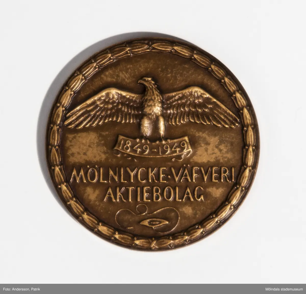 Minnesmynt i brons från Mölnlycke väfveri AB, utgivet 1849-1949.

Minnesmyntet ligger i en grön orginalförpackning. Förpackningen är av papp. På undersidan finns texten: "C.C. SPORRONG & CO. KUNGSGATAN 17. STOCKHOLM". 
På myntets ena sida finns en örn med texten "1849-1949 MÖLNLYCKE VÄFVERI AKTIEBOLAG" gjutet i myntet. 
På andra sidan finns Mölnlycke väfveri och Krokslätts fabriker gjutna.