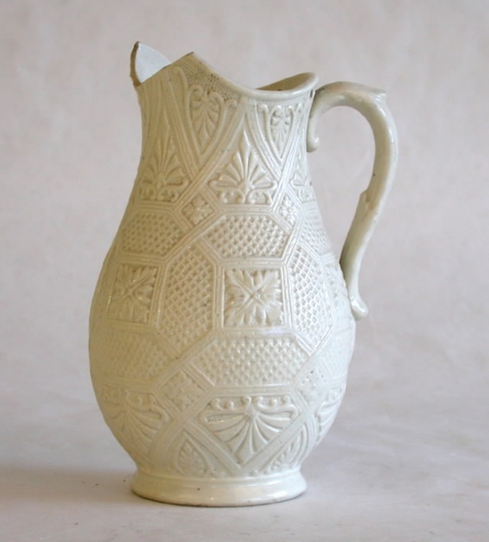 Vit tillbringare av fajans. Pip defekt. Stiliserad bladdekor i relief.