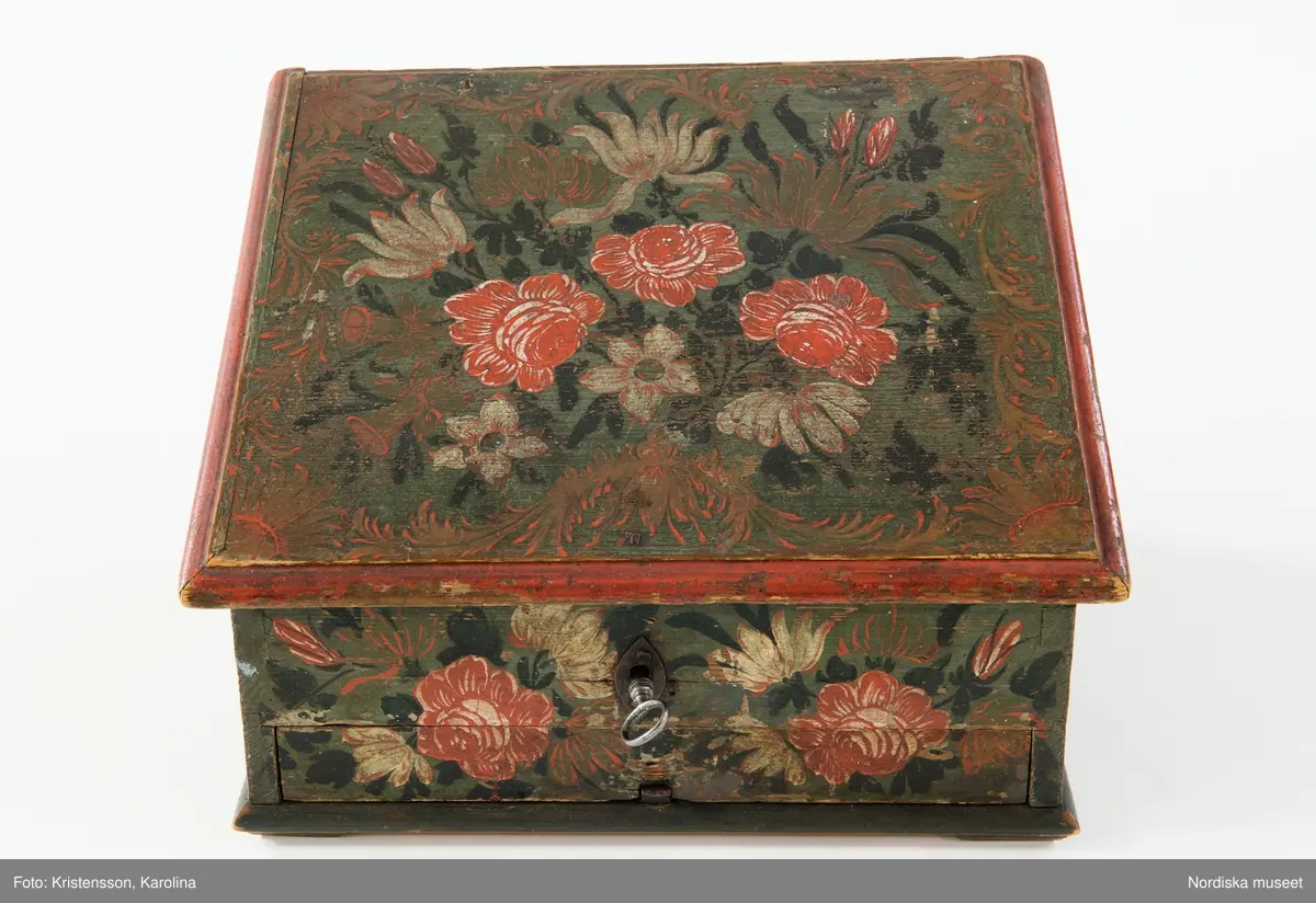 Inventering Sesam 1997-1998:
B 30, Djup 23,5, H 20 cm
Skrin, nästan kvadratiskt, med pulpetlock, av barrträ. Utanpåliggande botten, fästad underifrån med skruvar (antagligen senare ditsatt). Sidorna ihopfogade genom sinkning.
Locket har skurna profillister limmade på kanterna, två enkla gångjärn fästade invändigt.
Utanpåliggande lås, låssprint av järn i locket, nyckelskylt av järn, med nyckel.
Låda som drags ut på framsidan, limmad botten, sinkade hörn, avdelad i sex fack, handtag av järnband fästat runt bottenkanten.
Utvändigt målad blomsterdekor på locket och samtliga sidor i rött, vitt, grönt och svart på blå botten, lådans förstycke målat i samma färger för att passa in med dekoren på framsidan.
Invändigt målat i vitt, locket med växtmotiv i gult samt " CJD 1791 ", även lådan vitmålad invändigt.
Skrinet har låga, trekantiga fötter av trä limmade i hörnen under botten.
Lådans botten spräckt på två ställen.
Enligt huvudliggaren innehöll skrinet en ring, två par handskar och två böcker (inv.nr. 258.413-416).
Agnetha Blomberg 1998