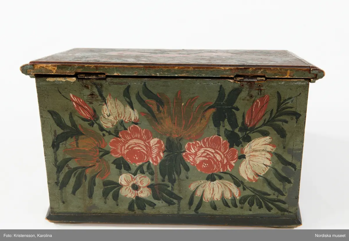 Inventering Sesam 1997-1998:
B 30, Djup 23,5, H 20 cm
Skrin, nästan kvadratiskt, med pulpetlock, av barrträ. Utanpåliggande botten, fästad underifrån med skruvar (antagligen senare ditsatt). Sidorna ihopfogade genom sinkning.
Locket har skurna profillister limmade på kanterna, två enkla gångjärn fästade invändigt.
Utanpåliggande lås, låssprint av järn i locket, nyckelskylt av järn, med nyckel.
Låda som drags ut på framsidan, limmad botten, sinkade hörn, avdelad i sex fack, handtag av järnband fästat runt bottenkanten.
Utvändigt målad blomsterdekor på locket och samtliga sidor i rött, vitt, grönt och svart på blå botten, lådans förstycke målat i samma färger för att passa in med dekoren på framsidan.
Invändigt målat i vitt, locket med växtmotiv i gult samt " CJD 1791 ", även lådan vitmålad invändigt.
Skrinet har låga, trekantiga fötter av trä limmade i hörnen under botten.
Lådans botten spräckt på två ställen.
Enligt huvudliggaren innehöll skrinet en ring, två par handskar och två böcker (inv.nr. 258.413-416).
Agnetha Blomberg 1998