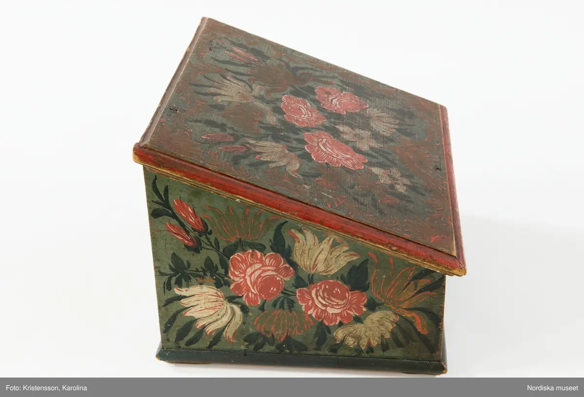 Inventering Sesam 1997-1998:
B 30, Djup 23,5, H 20 cm
Skrin, nästan kvadratiskt, med pulpetlock, av barrträ. Utanpåliggande botten, fästad underifrån med skruvar (antagligen senare ditsatt). Sidorna ihopfogade genom sinkning.
Locket har skurna profillister limmade på kanterna, två enkla gångjärn fästade invändigt.
Utanpåliggande lås, låssprint av järn i locket, nyckelskylt av järn, med nyckel.
Låda som drags ut på framsidan, limmad botten, sinkade hörn, avdelad i sex fack, handtag av järnband fästat runt bottenkanten.
Utvändigt målad blomsterdekor på locket och samtliga sidor i rött, vitt, grönt och svart på blå botten, lådans förstycke målat i samma färger för att passa in med dekoren på framsidan.
Invändigt målat i vitt, locket med växtmotiv i gult samt " CJD 1791 ", även lådan vitmålad invändigt.
Skrinet har låga, trekantiga fötter av trä limmade i hörnen under botten.
Lådans botten spräckt på två ställen.
Enligt huvudliggaren innehöll skrinet en ring, två par handskar och två böcker (inv.nr. 258.413-416).
Agnetha Blomberg 1998