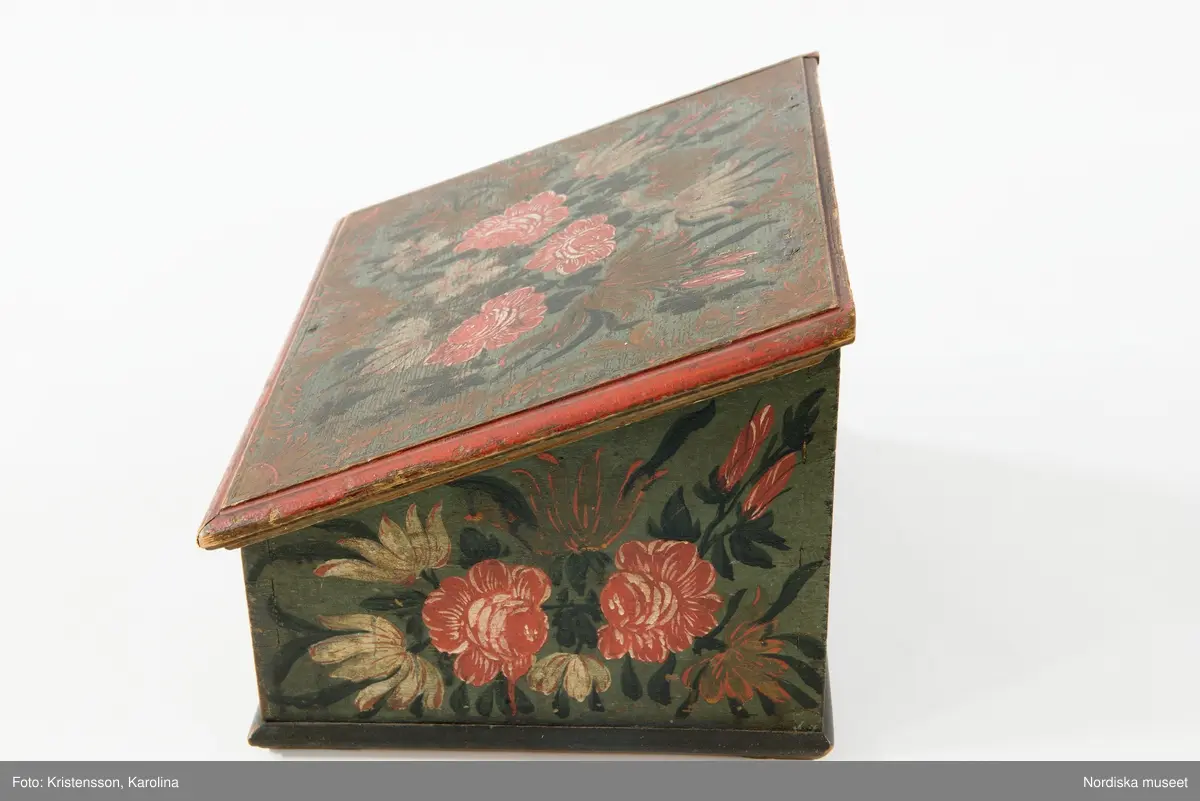 Inventering Sesam 1997-1998:
B 30, Djup 23,5, H 20 cm
Skrin, nästan kvadratiskt, med pulpetlock, av barrträ. Utanpåliggande botten, fästad underifrån med skruvar (antagligen senare ditsatt). Sidorna ihopfogade genom sinkning.
Locket har skurna profillister limmade på kanterna, två enkla gångjärn fästade invändigt.
Utanpåliggande lås, låssprint av järn i locket, nyckelskylt av järn, med nyckel.
Låda som drags ut på framsidan, limmad botten, sinkade hörn, avdelad i sex fack, handtag av järnband fästat runt bottenkanten.
Utvändigt målad blomsterdekor på locket och samtliga sidor i rött, vitt, grönt och svart på blå botten, lådans förstycke målat i samma färger för att passa in med dekoren på framsidan.
Invändigt målat i vitt, locket med växtmotiv i gult samt " CJD 1791 ", även lådan vitmålad invändigt.
Skrinet har låga, trekantiga fötter av trä limmade i hörnen under botten.
Lådans botten spräckt på två ställen.
Enligt huvudliggaren innehöll skrinet en ring, två par handskar och två böcker (inv.nr. 258.413-416).
Agnetha Blomberg 1998