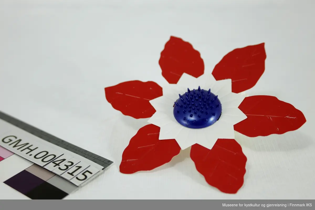 Blomsten består av to lag papp. Det nederste laget er utformet som seks blader og er rødt. På det er det et mindre lag av hvit papp med en sikksakk-kant. Begge lag holdes sammen av et blå plastelement med nubber på.