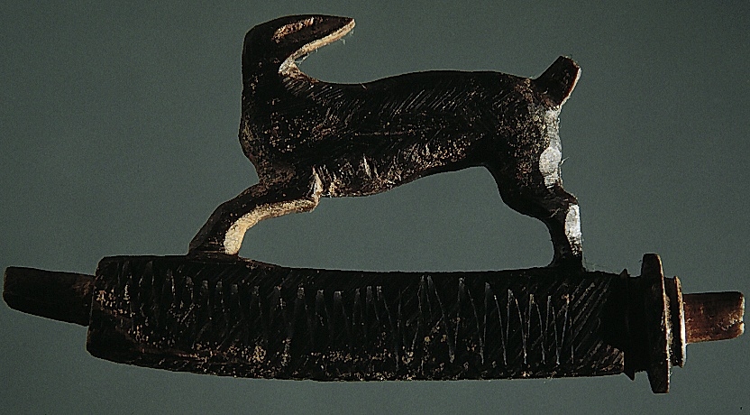 Snidad djurfigur. Basen som djuret står på har kvadratiskt tvärsnitt. Genom basen löper ett ihåligt rör. Djurfiguren föreställer en löpande hare, hjort eller hund. Djurhuvudet är avbrutet.
