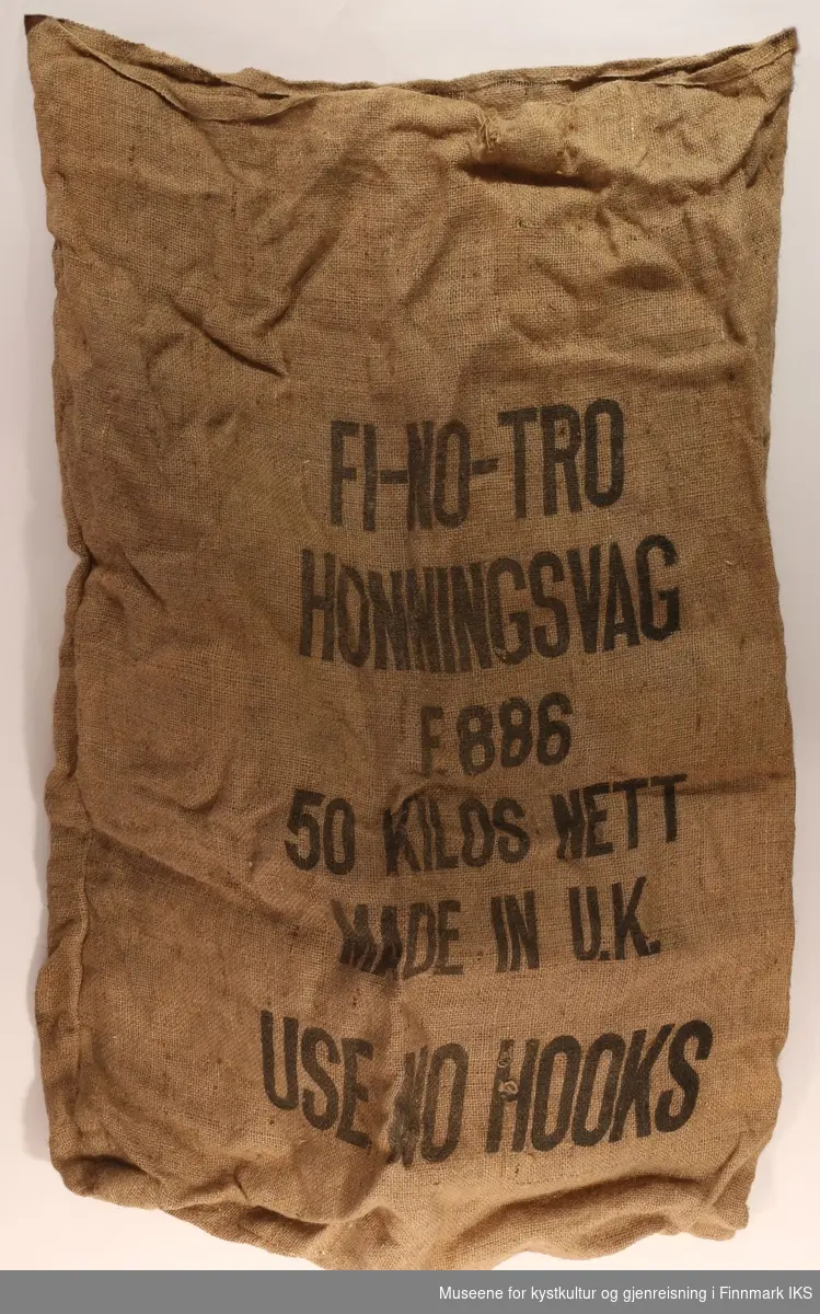 En striesekk med tekstiltrykk. 

På sekken er det trykt "FI-NO-TRO HONNINGSVAG, F.886, 50 KILOS NETT, MADE IN U.K, USE NO HOOKS".
