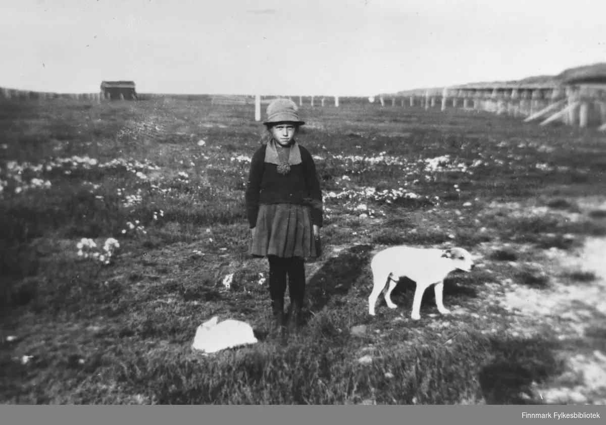 Yngstejenta Aud og hunden Flink på jordet 1922 i bakgrunnen sommerfjøset. Familien eide store landområder i Kongsfjord. Jorda som tilhører hovedhuset, ble senere solgt (ca. 1960).