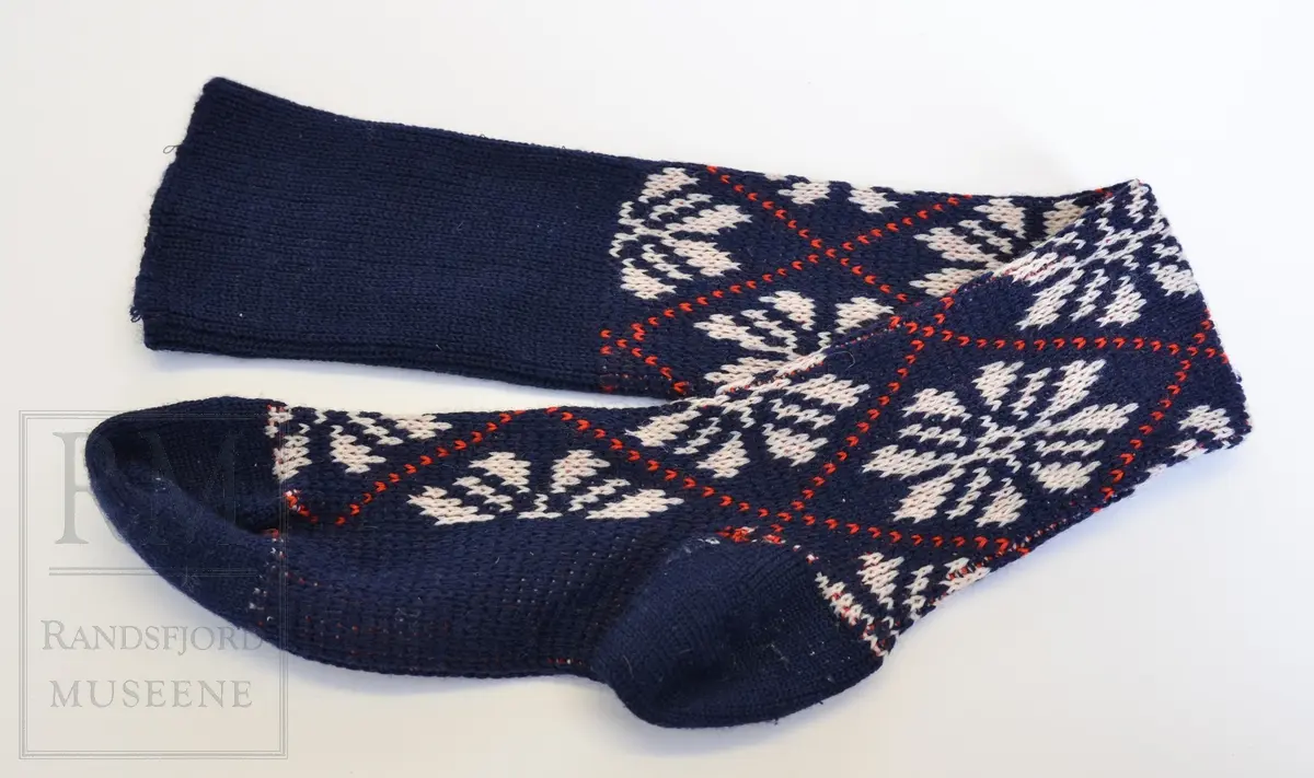 Knestrømper, mønstrede, maskinstrikket, til bruk sammen med knikkers. Herremodell. Ull og kunstfiber. Blå med hvite stjerner/roser og røde striper i rutemønster. Elastikk.