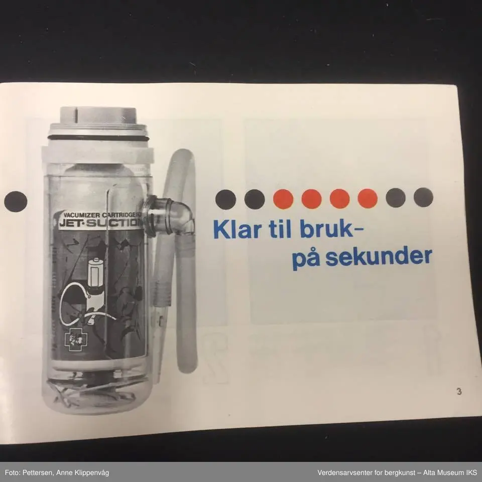 A. Sylinderformet plastapparat med tilfestet gummislange og gjennomsiktig plasttut.  Inneholder en driftspatron fylt med ufarlig gass.
B Rektangulært hefte, bruksanvisning.