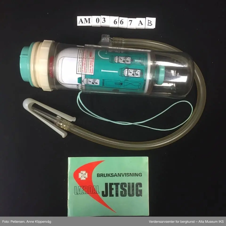 A. Sylinderformet plastapparat med tilfestet gummislange og gjennomsiktig plasttut.  Inneholder en driftspatron fylt med ufarlig gass.
B Rektangulært hefte, bruksanvisning.