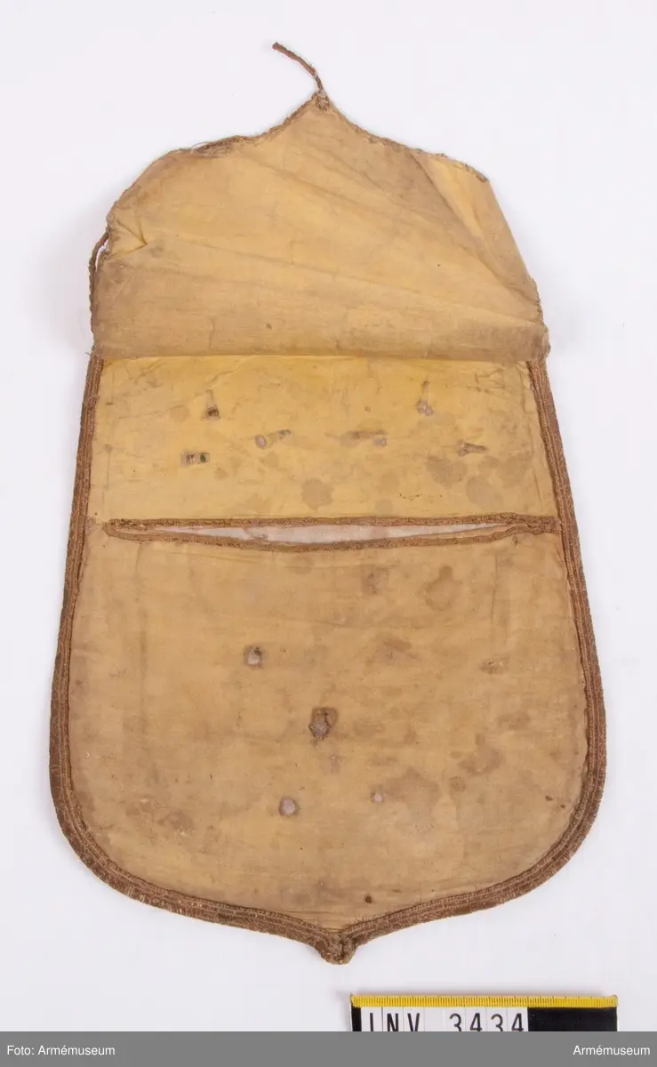 Monogram Oscar I.
Mått: 265 x 220 mm.
Framsidan är täckt  med ett ganska tunt ylletyg, vävt i kypert. Locket är kantat  med ett band i guldgalon. Innanför bandet är som dekoration fastsytt ett mycket smalt guldband, som endast är kvar på ena  sidan och upptill och vid den andra sidan är helt borta. På  mitten av locket är ett 90 mm högt monogram för Oscar I, däröver två öppna kronor och under monogrammet en Öppen krona. Locket är fodrat med ett ljusgult bomullsfoder vävt i tuskaft. Färgen skall väl vara saffianliknande (= marokäng eller saffian, mjukt läder av get eller bockskinn). En ficka finnes på mitten av fodersidan och sträcker sig tvärs  över från sida till sida och går på djupet till lockets nedersta kant. Över ficköppningen fälles ett lock, kantat med  guldband och upptill fastsatt under den guldgalon som går runt  lockets kant. Vilket regemente som haft detta lock med detta utseende vet jag  just nu inte, men gissar på, som hade mörkblå sabeltaska med gul saffian tiden 1814-54. Kanske är det teaterrekvisita? Åke Dalbeck tror "barnleksak" f kungl. barn.