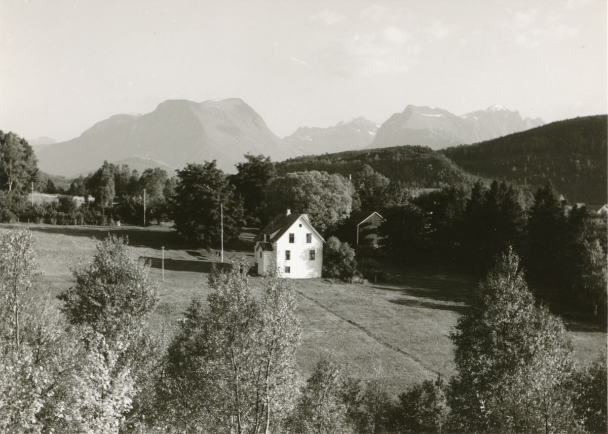 Gårdstun med skog omkring i Solavågen. Utsikt mot Hjørundfjordfjella.