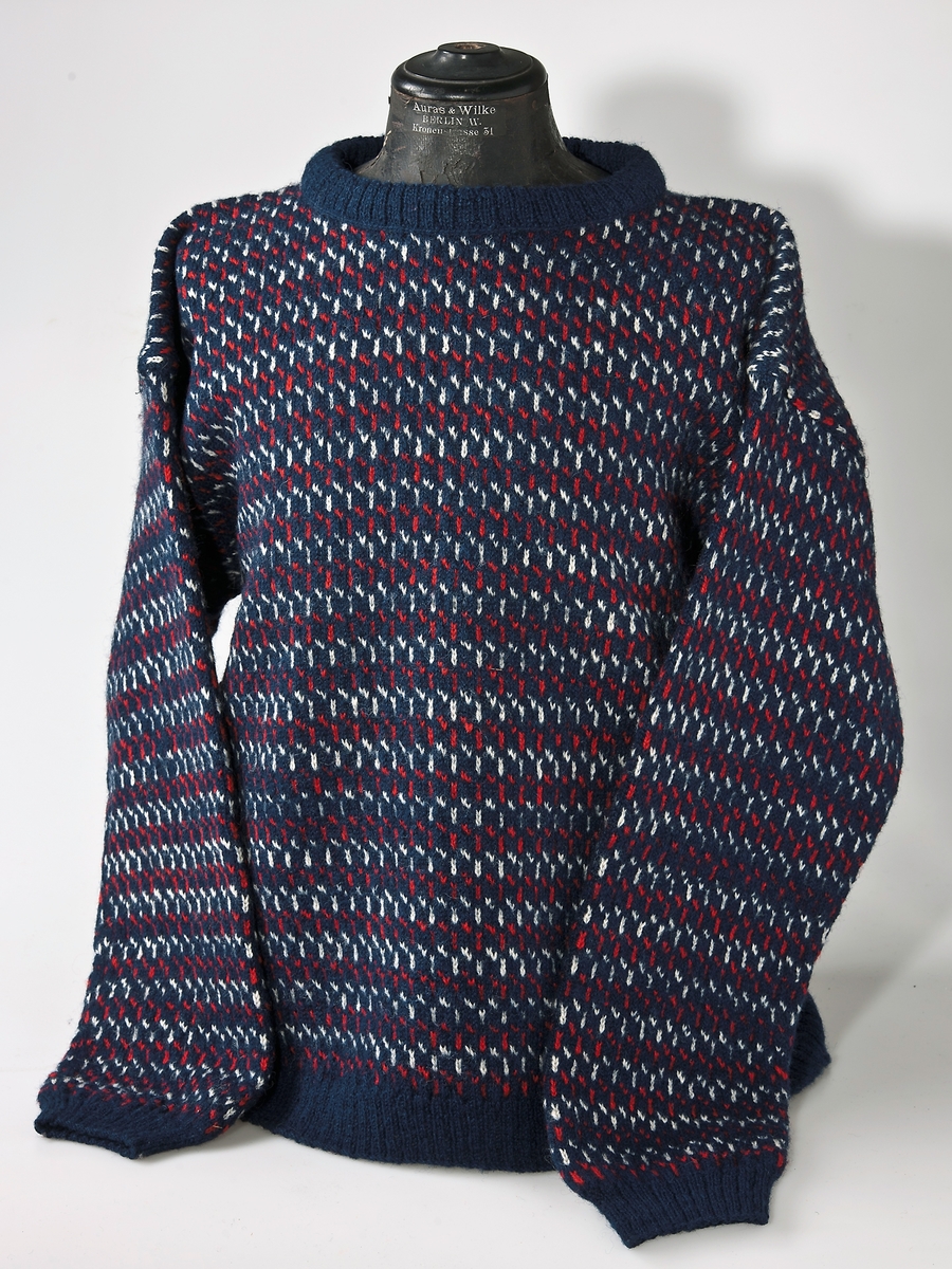 Bingestickad tröja i 2-trådigtullgarn. 
Rött och vitt mönster på blå botten. 
Resårstickad nederkant, ärmmuddar och halskant