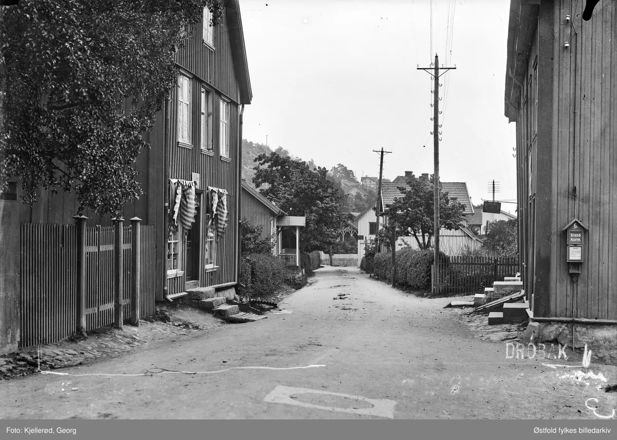 Fra Storgata i Drøbak. 

Storgata 18, smed Evensengården, revet i 1968-69 til venstre. Videre nedover gaten på venstre side ser vi Sørbyhuset, revet 1968-69. 

Til høyre ser vi hjørnet av Storgata 15, tidligere slakter Abrahamsen. Slakterbutikken fikk etterhvert inngang på hjørnet, og er fremdeles synlig med okse over døren og oksebein på begge siden av døren. Skåret av treskjærer og skiltmaker John Jul Jensen, Drøbak.

Forretning til venstre med skilt : I. Nilsen. Ant bakeri bygning til høyre.