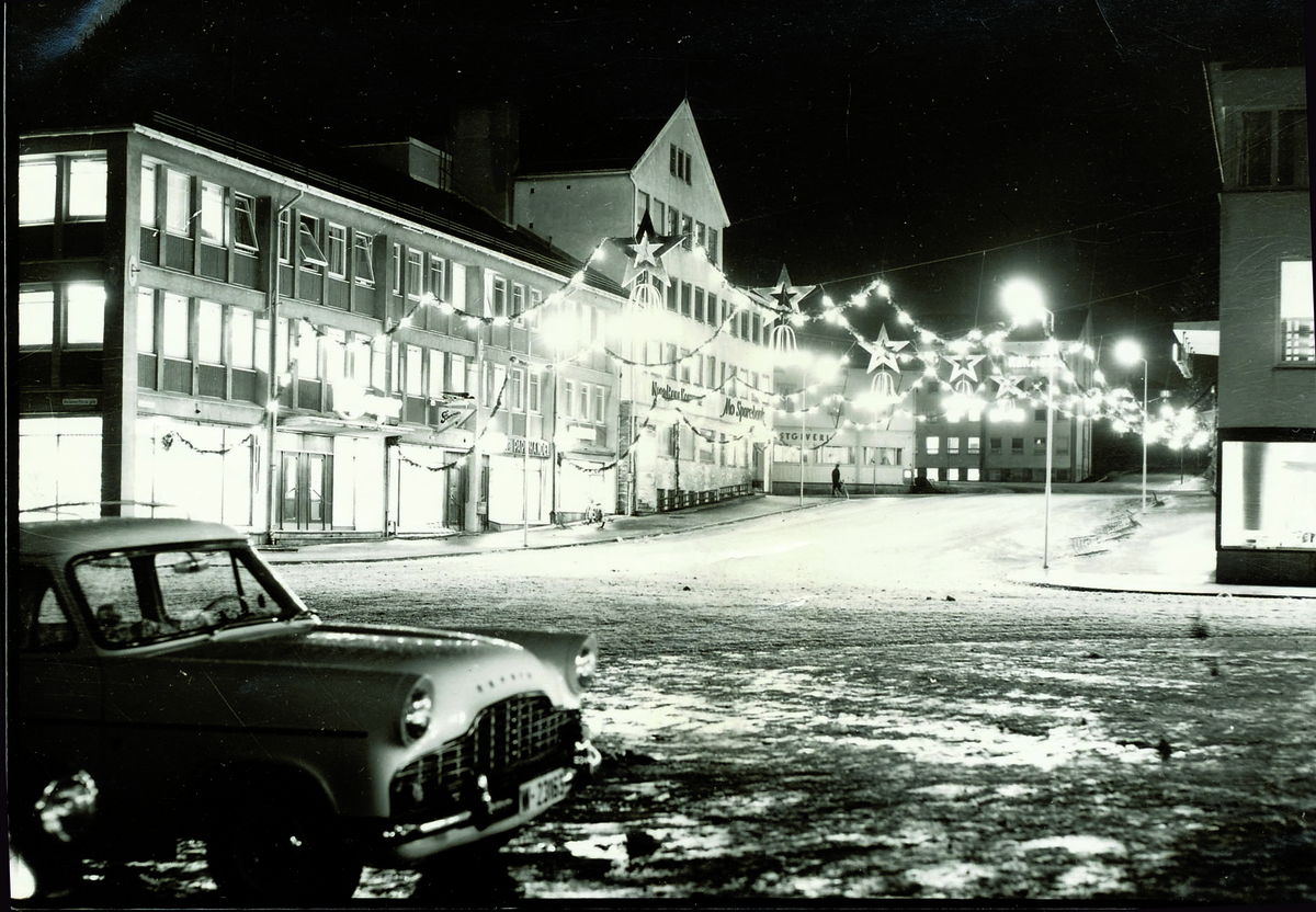 Julegate mellom Meyers varehus og Rana Samvirkelags varehus i Mo sentrum. Bil parkert i forgrunnen.