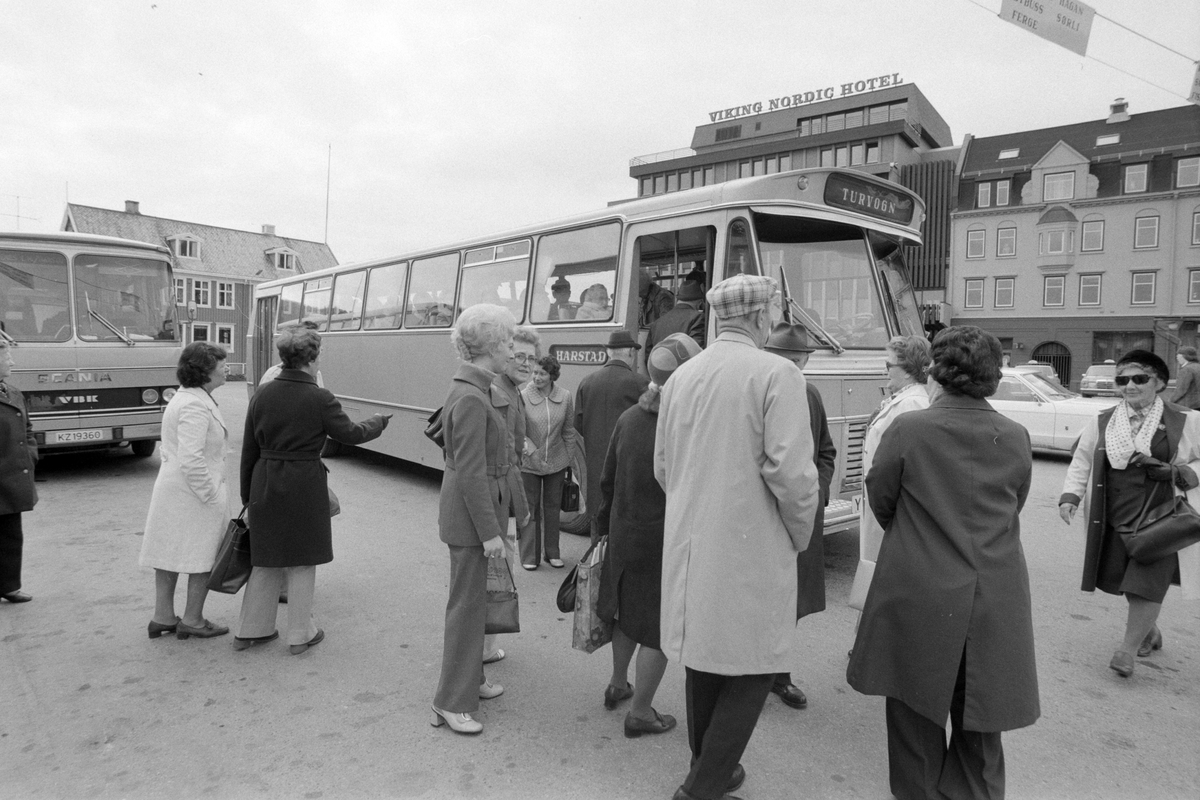 Turbuss på rutebilstasjonen i sentrum. Ventende passasjerer i forgrunnen.