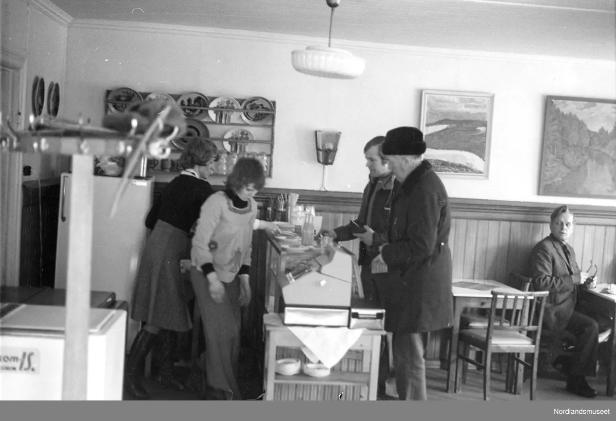 Rognan sentrum en lørdag formiddag. Kaféliv. Erling Engan, Senterpartiet blir servert ved disken. 5 personer med på bildet. Fritz Andersen står ved siden av Erling Engan ved disken der, han som sitter ved bordet og snur seg mot disken er Kulseth, fornavn ukjent.