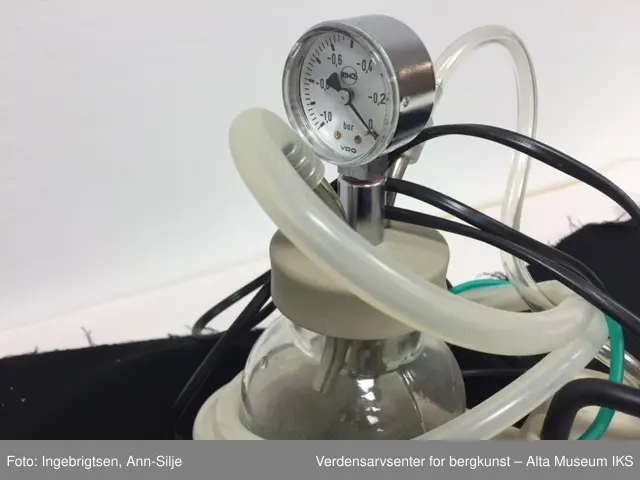 Rektangulært apparat med avrundet sokkel med en sylinderformet glasskolbe i. På lokket til glasskolben er det en trykkmåler og to metalltuter hvor det er festet en gummi/plastslange i hver. Den ene slangen går inn i selve apparatet og den andre er kveilet rundt glasskolben. Glasskolben er merket med grønne streker og tall. På venstre siden av apparatet er det en av- og på-knapp. Bruksområdet er å suge opp væske, særlig i fra luftveiene.