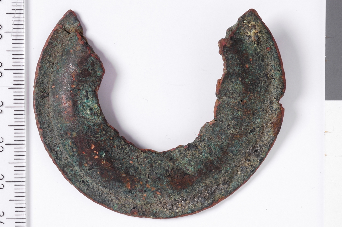 Sirkelformet metallplate med jevn ytterkant og en bruddfalte klangs hele innsiden, samt i begge kortender. det er ingen tegn til dekor, men platen er flat i ytterkant og har deretter en konveks bue som går innover. Dette er et kraftig beslag, men med ukjent bruksområde.