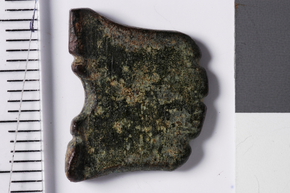 Tilnærmet firkantet gjenstand med en halvsirkelformet fordypning i den tykkeste enden. Denne enden fungerer som en "fot" som gjør at gjenstanden står stabilt oppreist. Tykkelsen er avsmalnende opp fra foten. Alle sider er intakte og toppen, dvs motsatt ende av foten, er bearbeidet med tre fordypninger som gir en bølgeform. Midt i overflaten av gjenstanden, rett over buen, sees på den ene siden rester av en fordypning som kan ha vært et preg. Kan være en spillebrikke.