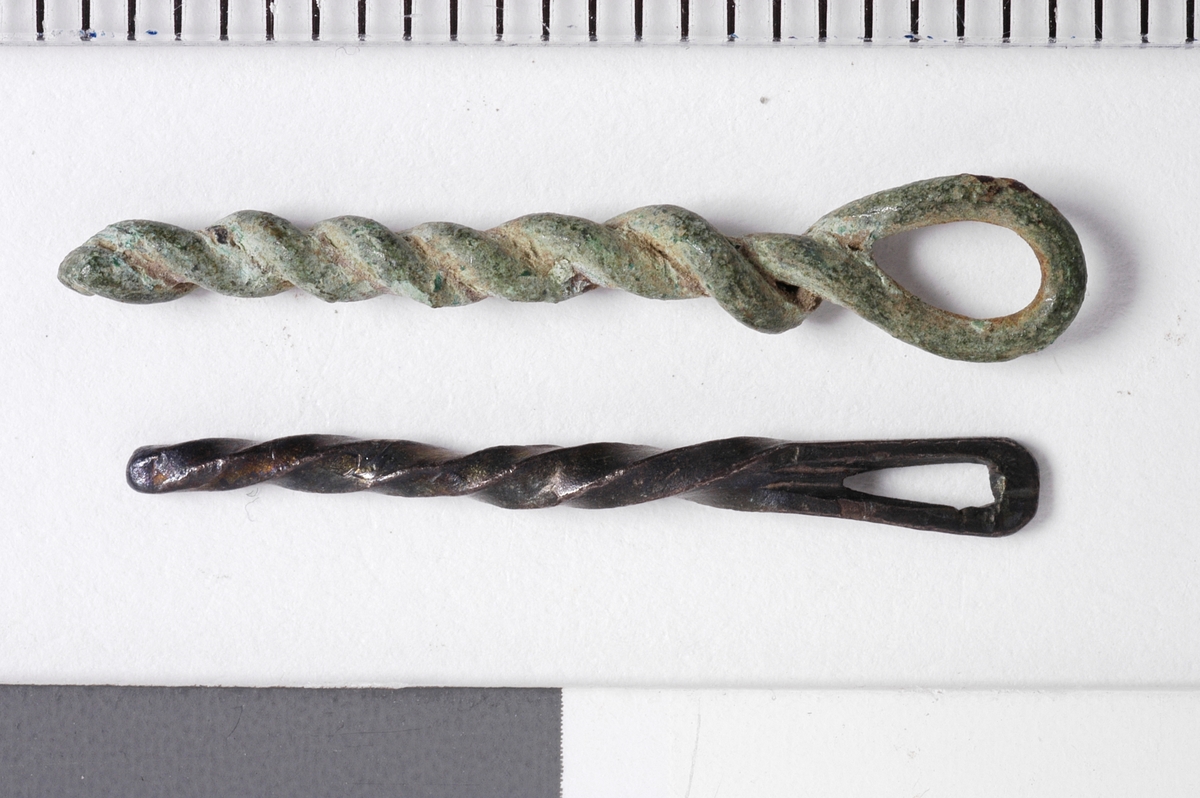 MALV: SE BESK., ST. L. 45 MM, MINSTE L. 16 MM, ST. DIAM. 2 MM, MINSTEDIAM. 1 MM. LAGET AV METALLTRÅD. GJENSTANDEN DANNET VED AT TYNNMETALLTRÅD (DIAM. 0, 5-1, 1 MM) ER LAGT DOBBEL OG SNODD I SPIRAL. ØYE IENDEN. NB! 2 HAR FLATTRYKT PARTI VED HULLET. 
