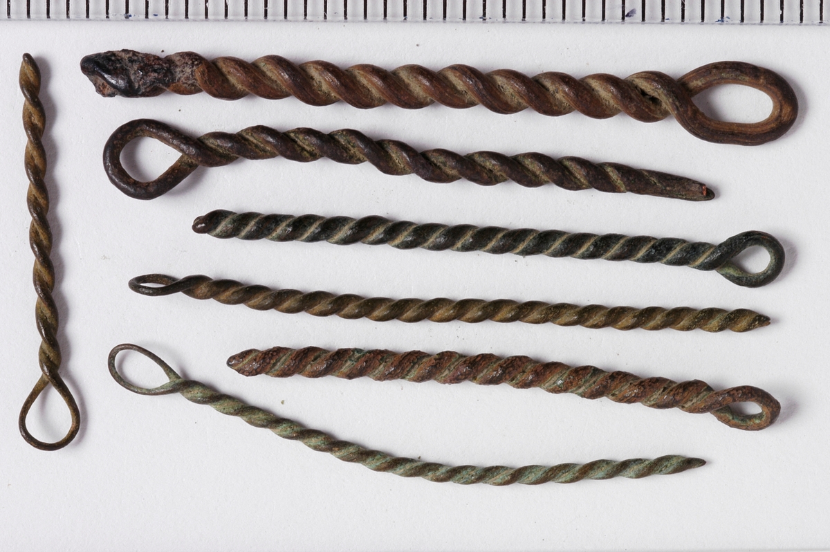 MALV: SE BESK., ST. L. 45 MM, MINSTE L. 16 MM, ST. DIAM. 2 MM, MINSTEDIAM. 1 MM. LAGET AV METALLTRÅD. GJENSTANDEN DANNET VED AT TYNNMETALLTRÅD (DIAM. 0, 5-1, 1 MM) ER LAGT DOBBEL OG SNODD I SPIRAL. ØYE IENDEN. NB! 2 HAR FLATTRYKT PARTI VED HULLET. 
