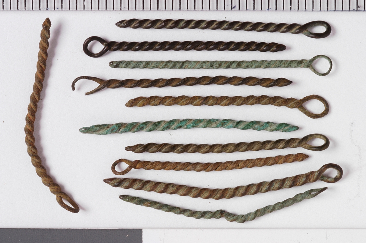 MALV: SE BESK., ST. L. 45 MM, MINSTE L. 16 MM, ST. DIAM. 2 MM, MINSTEDIAM. 1 MM. LAGET AV METALLTRÅD. GJENSTANDEN DANNET VED AT TYNNMETALLTRÅD (DIAM. 0, 5-1, 1 MM) ER LAGT DOBBEL OG SNODD I SPIRAL. ØYE IENDEN. NB! 2 HAR FLATTRYKT PARTI VED HULLET. 