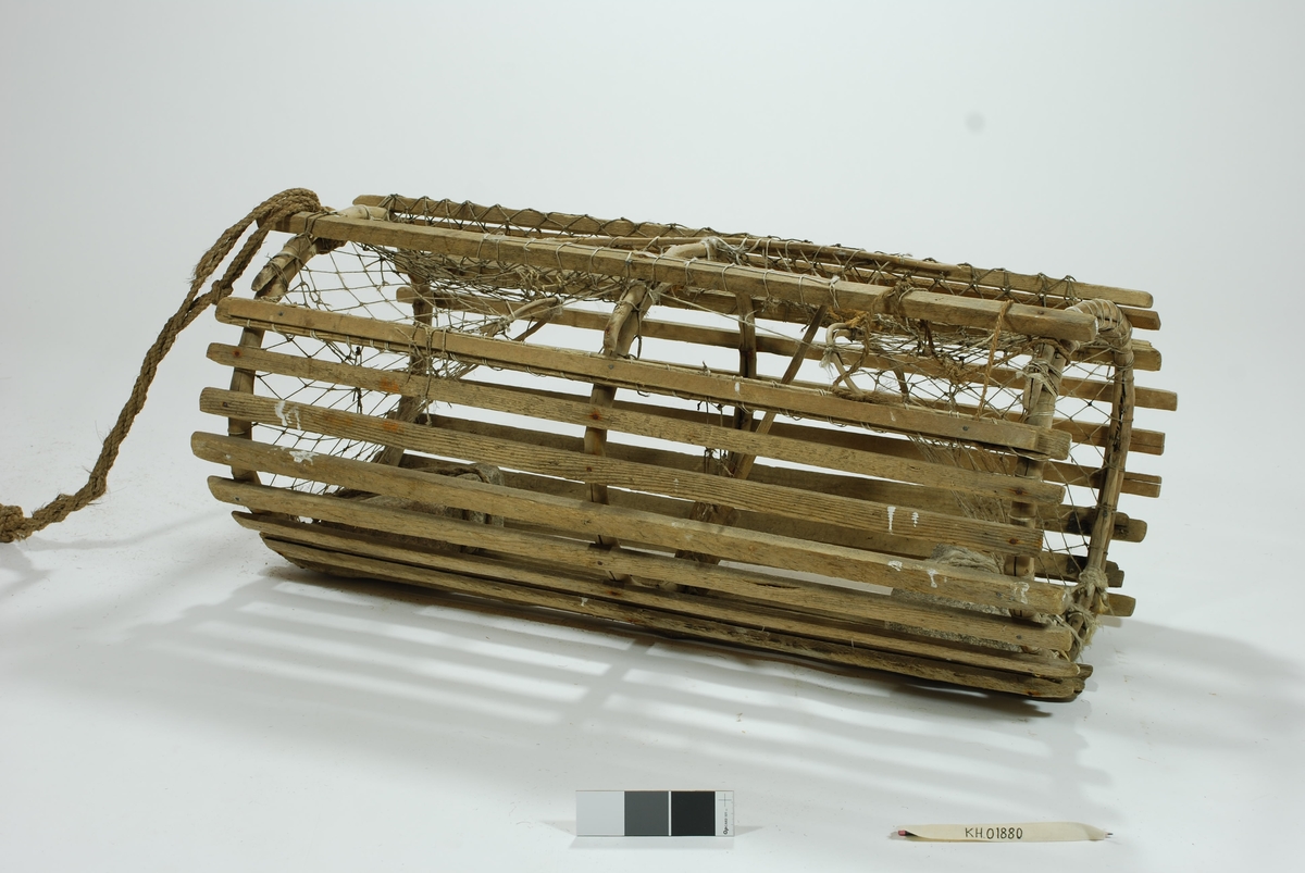 Moderat stor sylindrisk tene med inngang i begge ender. Lekter i ulike dimensjoner. Gjorderinger av ener.  Midterste gjordering sprukket. Kalveringer av ener. Kalver i hvitt garn. Reparasjoner i begge kalvene. Garnbusen på toppen i et litt kraftigere tau. Slitt av flere steder. Reparasjoner/fester med gresstau og hvitt tau (kokos?). 
Lukkeåpning i garn med håndsnittet trepinne. Agnspyd i tre. Festet til midterste gjordering med gresstau. Synkestener av granitt, en i hver ende. Den ene festet med hvitt tau (kokos?), den andre med et tykkere gresstau. Har ikke gummi/deler av regntøy til beskyttelse som en rekke andre tener har. Bunnsvillene/lektene forsterket for stabilitet ved bunn-leie. Langt gresstau festet til. Uten væler.