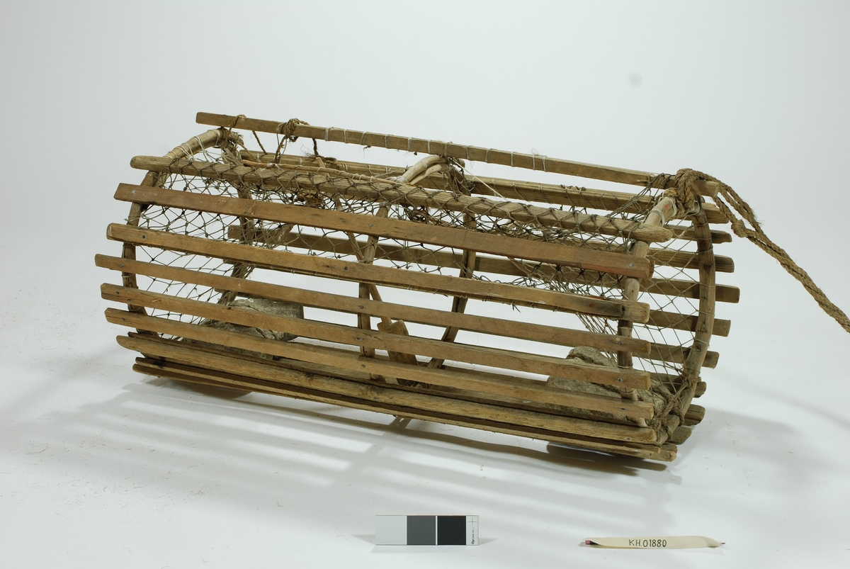 Moderat stor sylindrisk tene med inngang i begge ender. Lekter i ulike dimensjoner. Gjorderinger av ener.  Midterste gjordering sprukket. Kalveringer av ener. Kalver i hvitt garn. Reparasjoner i begge kalvene. Garnbusen på toppen i et litt kraftigere tau. Slitt av flere steder. Reparasjoner/fester med gresstau og hvitt tau (kokos?). 
Lukkeåpning i garn med håndsnittet trepinne. Agnspyd i tre. Festet til midterste gjordering med gresstau. Synkestener av granitt, en i hver ende. Den ene festet med hvitt tau (kokos?), den andre med et tykkere gresstau. Har ikke gummi/deler av regntøy til beskyttelse som en rekke andre tener har. Bunnsvillene/lektene forsterket for stabilitet ved bunn-leie. Langt gresstau festet til. Uten væler.