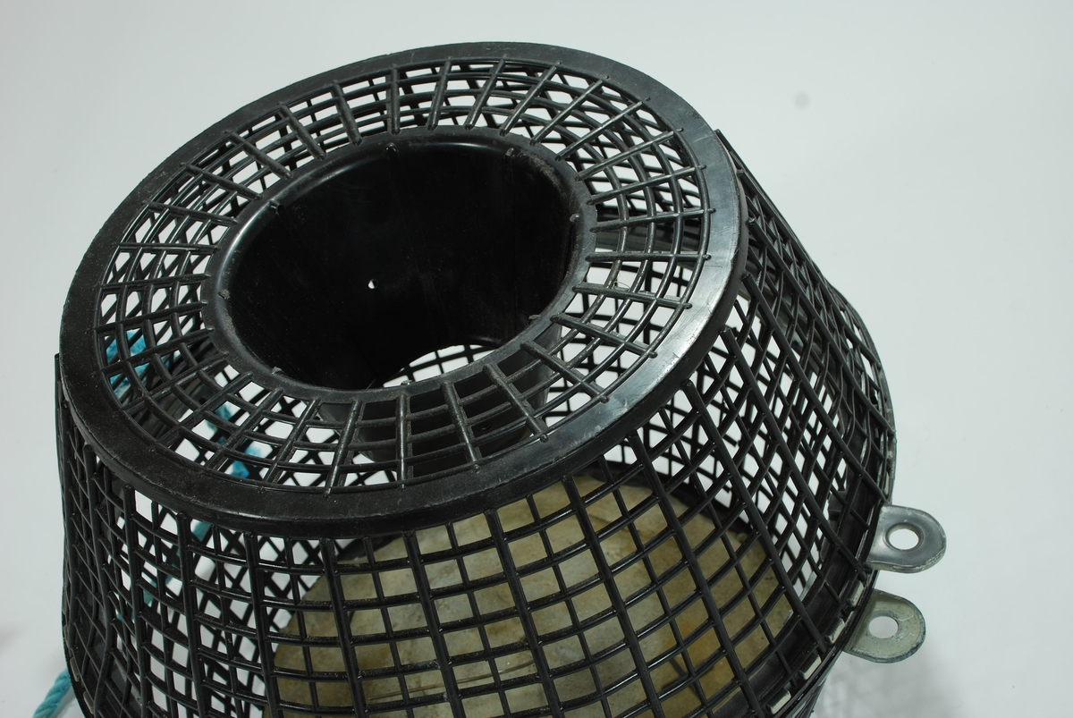 En forenklet versjon av de tradisjonelle fall-fellene hvor garnet er erstattet av hård-plast. Todelt bøtte-tene med topp og bunn. Form og materiale kan minne om en skittentøyskurv. 
Rutemønstret, sort hardplast. 
Betongblokk i bunnen til synkemateriale. Dekker hele bunnen. Små biter faller av i kantene.  Agnspyd av metall er støpt inni betongen. Fallbøtte i toppen. Både topp og bunn har randkant i hard gummi med tapper som vris i hverandre for å lukke tena. Turskis nylontau er festet i disse.