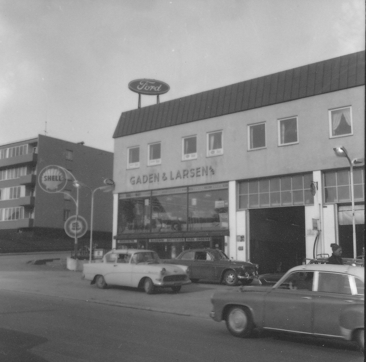 Forretningsbygg. Gaden & Larsen. Biler parkert på fortauene rundt.