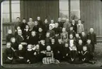 Andra klassen av Falköpings folkskola vårterminen 1900 utanför norra gavelväggen. Fotot taget av en resande fotograf. 1: Sahlkvist, Oskar, Agnestad 2: Nyberg, Karl, Hästhagen 3: Johansson, Gunnar, Blåsås 4: Frid, Tekla, Falköping5: Hofman, Klara, Gunnestorp 6: Gustavs, Anna, (stenk), Mossen 7: Andersson, Ruth, Falköping 8: Båth, Sven, Prästgatan 9: Hellström, Gustav, 10: Haglund, Olof, 11: Bengtsson, Gestrud, (Gertrud) ? 12: Svensson, Ivan, Gasvägen, 13: Hedbom, Emil, Forsens 14: Eriksson, Hildur, Banv, Sköttning 15: Jofur, Emma, 16: Gustafsson, Hanna, 17: Olsson, Anna, 18: Holm, Arvid, Banv, Sköttning 19: Sederholm, Karl, Annedal 20: Linnmann, Oskar, 21: Lärare Fast, J.A. 22: Holm, Anna Öfr. Gärdesgatan 23: Sand, Märtha, Storgatan 24: Syrén, Hilma, Bestorp 25: Karlsson, Anna, Öfr. Gärdesgatan 26: Hasselberg, Yngve, Sikagården 27: Larsson, Ferdinand, Öfr Gärdesgatan 28: Melin, Oskar, Nygatan 29: Andersson, Edit, Ledsgården, Bestorp 30: Vickström, Judith, Kyrkogatan 31: Olsson, Alma, Nygatan 32: Krall, Beda, S