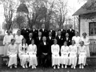 Konfirmander, 11 flickor, 11 pojkar och kyrkoherde Gabriel Carlsten.
Ekeby kyrka i bakgrunden.