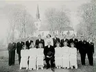 Kils kyrka i bakgrunden.
Konfirmander, 7 flickor, 9 pojkar och kyrkoherde Sköldebrand.