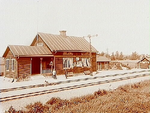 Tarsta Järnvägsstation, envånings stationsbyggnad.
Liten byggnad innehållande toaletter.
2 personer framför byggnaden.