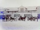 Stallbyggnad. Två hästdroskor med kuskar. En landå med en häst. En man med två hästar. En newfoundlandshund.
G. Sandholm