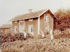 En och en halvvånings bostadshus (parstuga ?).
Familj 7 personer framför huset.
Gustaf Lindén