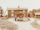 Tvåvånings bostadshus med veranda i snickarglädje. Lågt uthus.
Fyra vuxna och tre barn varav en på gunghäst.
Elof Bolinder