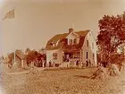 En och en halvvånings bostadshus med veranda, brutet tak, 2 st takhuvar, 2 mindre byggnader.
Ehrlings 60 årsdag. Födelsedagsgäster runt huset.
Ehrling