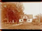 En och en halvvånings bostadshus med frontespis, balkong och förstebro.
Två kvinnor och en man framför huset.
Gustaf Bylow