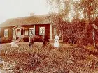 Envånings bostadshus med inredd vind, förstebro med snickarglädje. 
Fyra personer framför huset.
Organist Lindgren