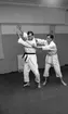 Judo 14 januari 1967

Två män i vita judodräkter tränar judo i en träningslokal. Mannen till vänster har svart bälte och mannen till höger har vitt bälte.