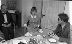 Inackorderingshem 27 april 1968

Två män och en kvinna sitter vid ett bord och pratar och dricker kaffe. På bordet ser man också vitsippor. Bakom 
dem står en tv med blommor på.