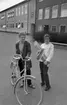 Vivalla problem, Trafiktävling, Konfirmation 10 maj 1966

Två unga tonårsflickor står på en skolgård. Flickan till vänster har kort hår och håller i en cykel. Hon är klädd i jacka, byxor och tröja och har ett halsband med en klocka på om halsen. Flickan till höger är klädd i vit kavaj, vit blus och mörka byxor. Hon håller i ett avlångt plastpaket. De står framför en skolbyggnad.