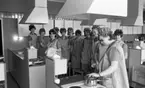 Yrkesskolan Älvtomta 25 april 1966

Kvinnor som går en yrkesutbildning i Älvtomta som berör ämnesområdet hushållskunskap står i ett kök. De är klädda i arbetskläder samt har likadana mössor på sina huvuden. De står samlade kring en spis samt en diskbänk. En av kvinnorna lyfter på locket till en kastrull och de andra betraktar detta.