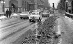 Vårregn, 31 januari 1966
Drottninggatan.
Bilar kör på gatan i centrala Örebro. I bakgrunden ligger Stora Hotellet. Det ligger snö på trottoaren. Tre herrar i mörka rockar och hattar syns i bakgrunden på bilden samt ytterligare personer längre bort.